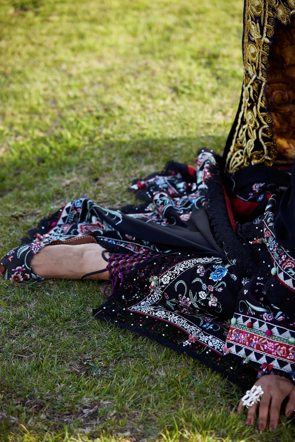 Person wearing a black embroidered outfit sitting on grass