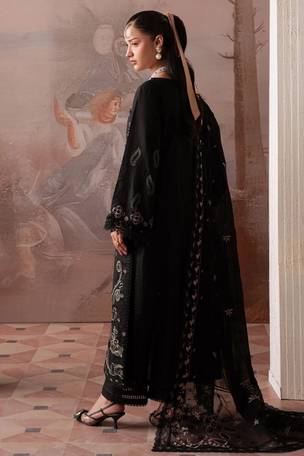 Woman in a black outfit with floral patterns standing in a room with classical painting.