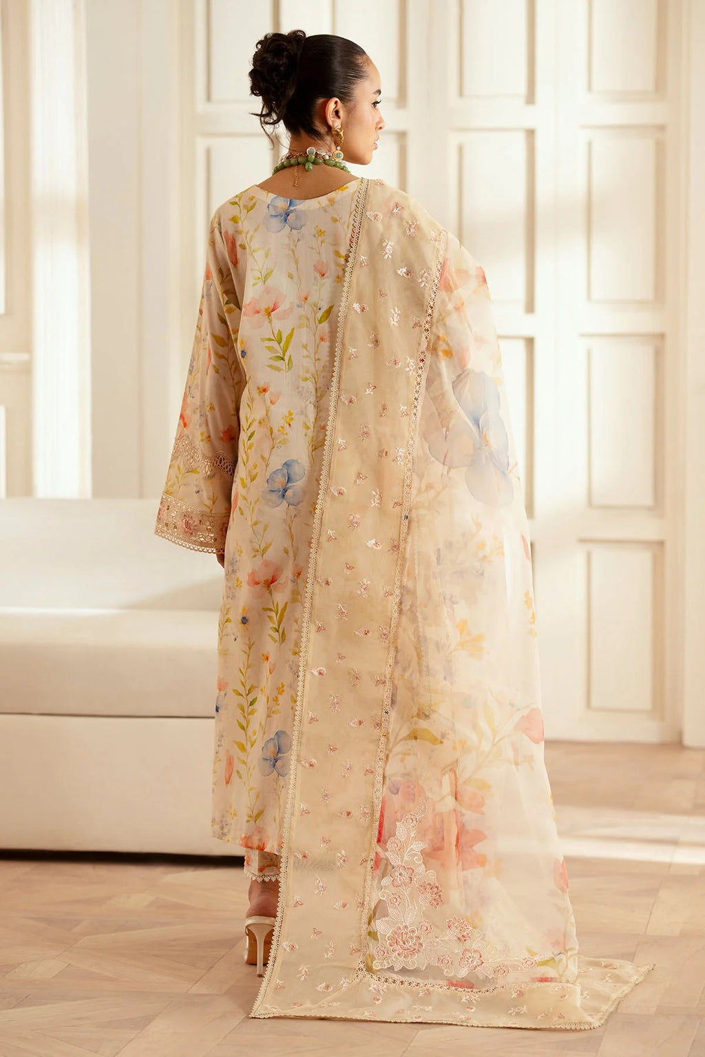 Woman wearing a floral outfit in a bright room with large windows.