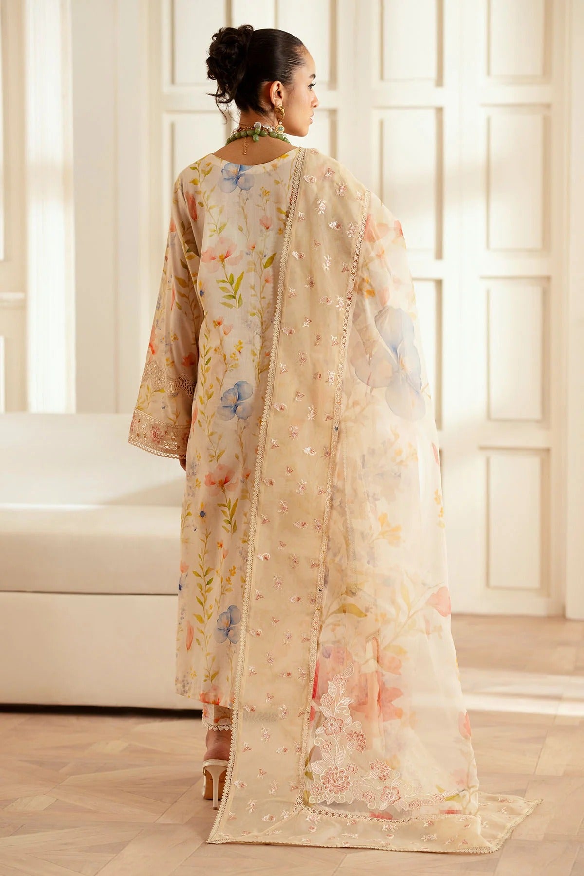 Woman wearing a floral outfit in a bright room with large windows.