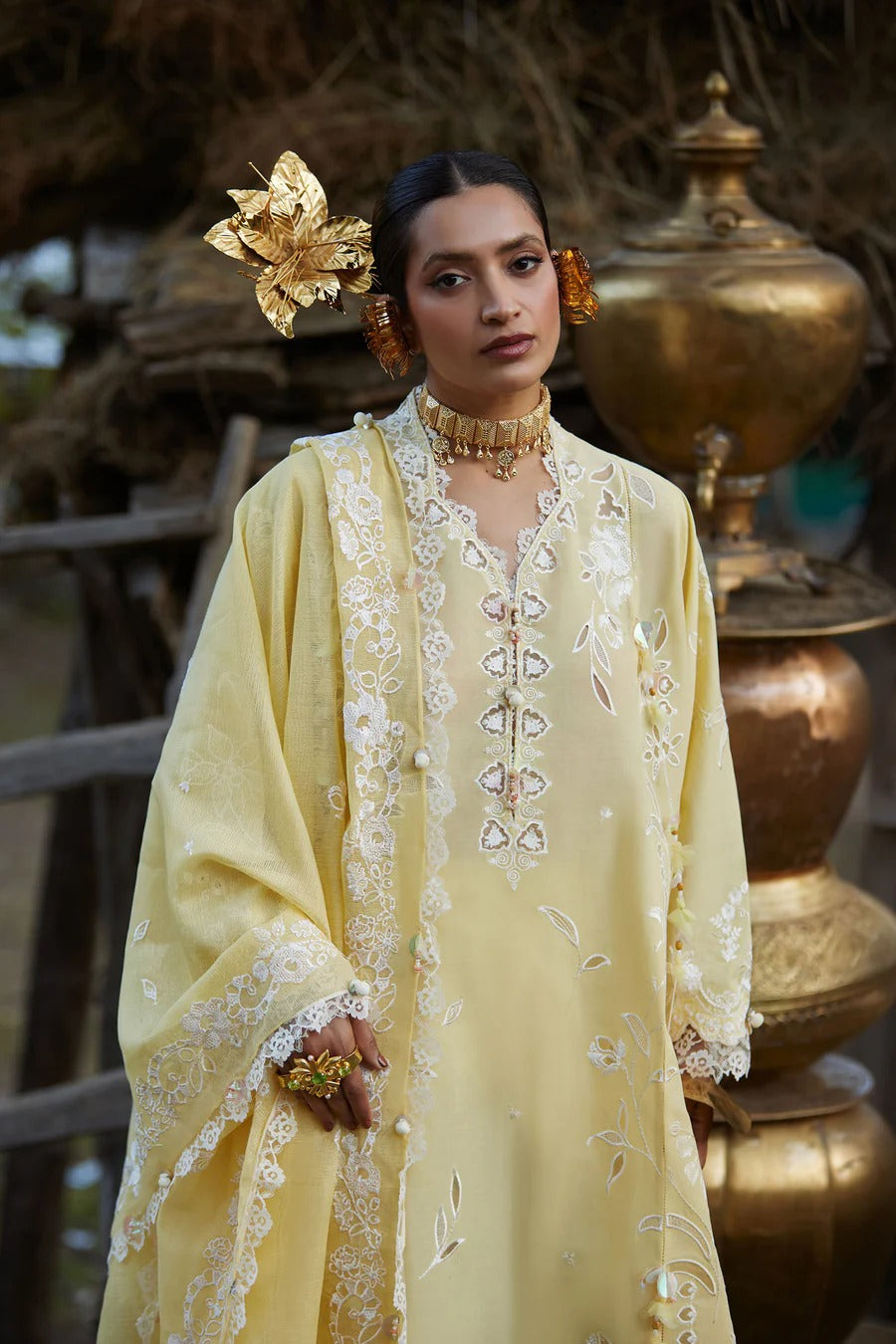 Woman in a yellow embroidered outfit with gold accessories in a rustic setting