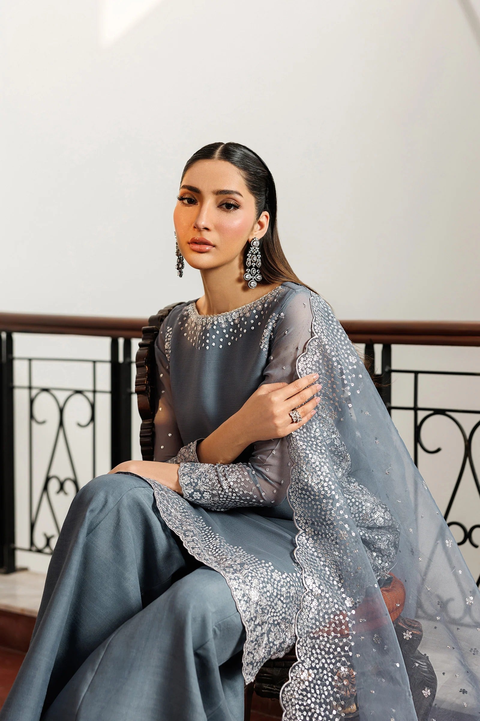 Woman in a gray traditional outfit with embellishments sitting indoors.