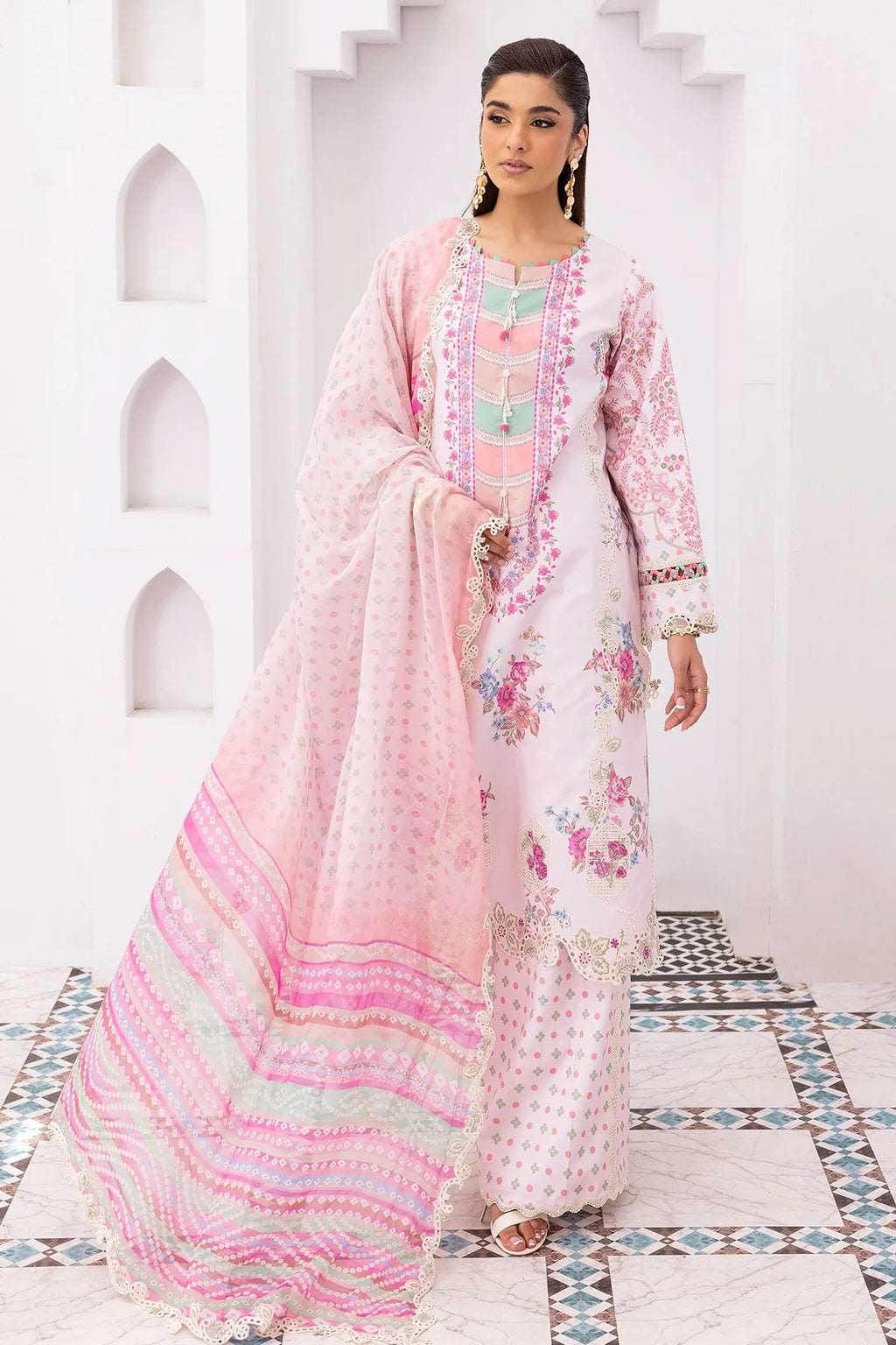 Woman wearing a pink and white traditional outfit with floral patterns in a decorative setting.