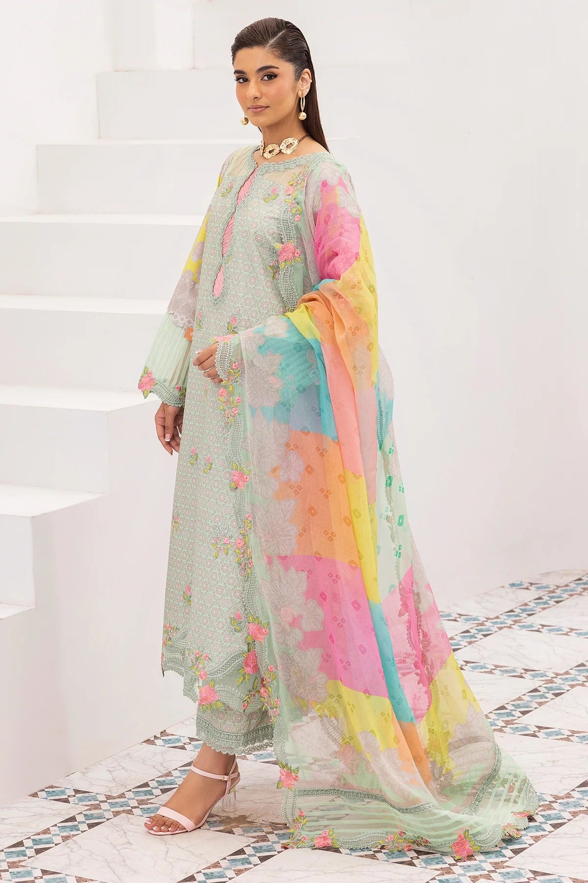 Woman in a colorful traditional outfit with a white staircase and patterned floor in the background