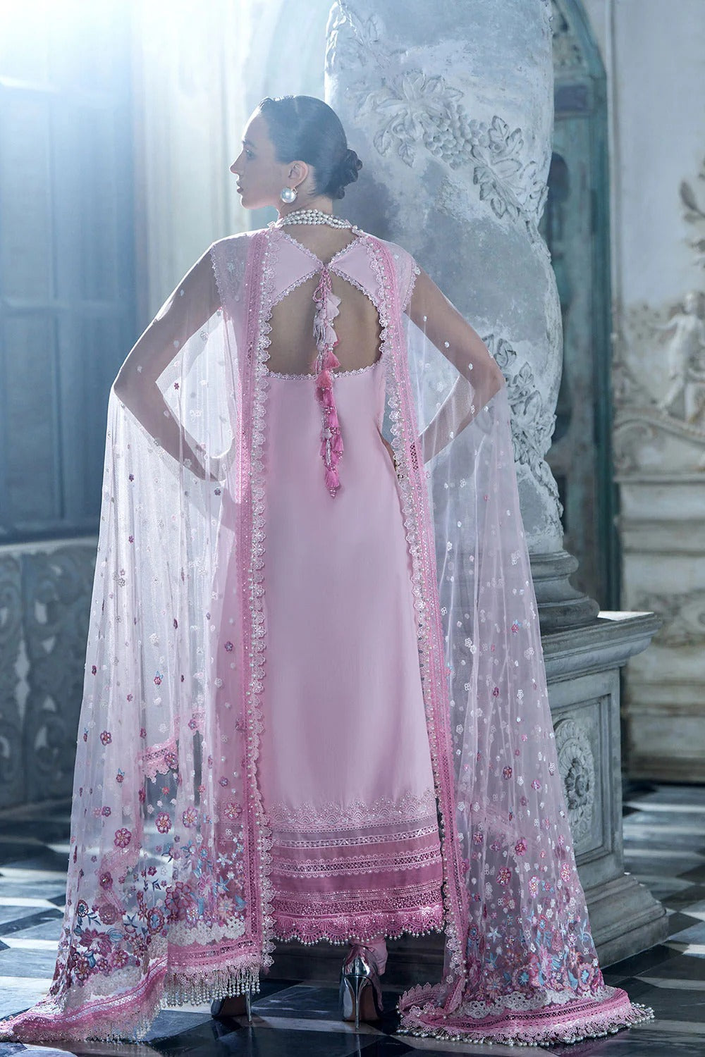 Woman in a pink traditional outfit with a floral cape in an elegant interior setting