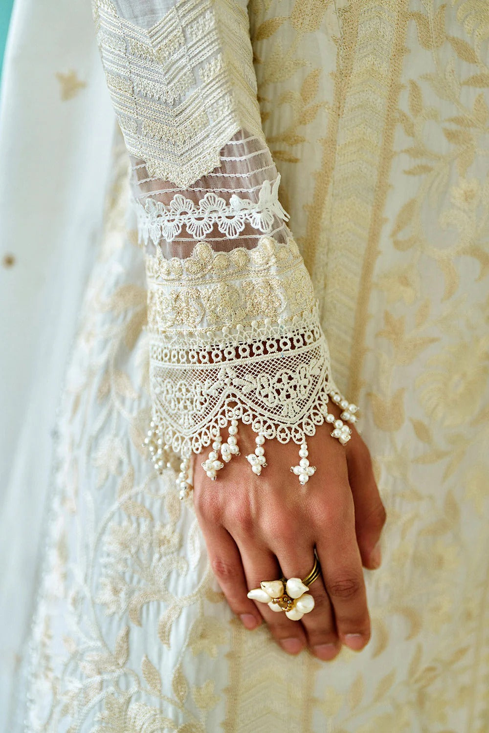 Close-up of a hand wearing a delicate lace glove with floral jewelry against a neutral background