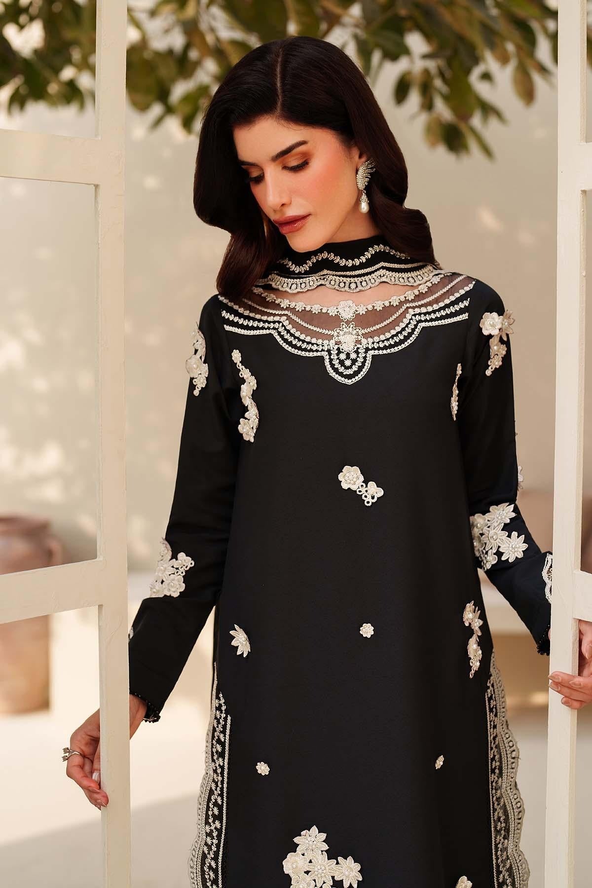 Woman wearing a black dress with white embroidery standing indoors.