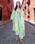 Woman in a light blue and green traditional outfit standing on a street with red buildings.