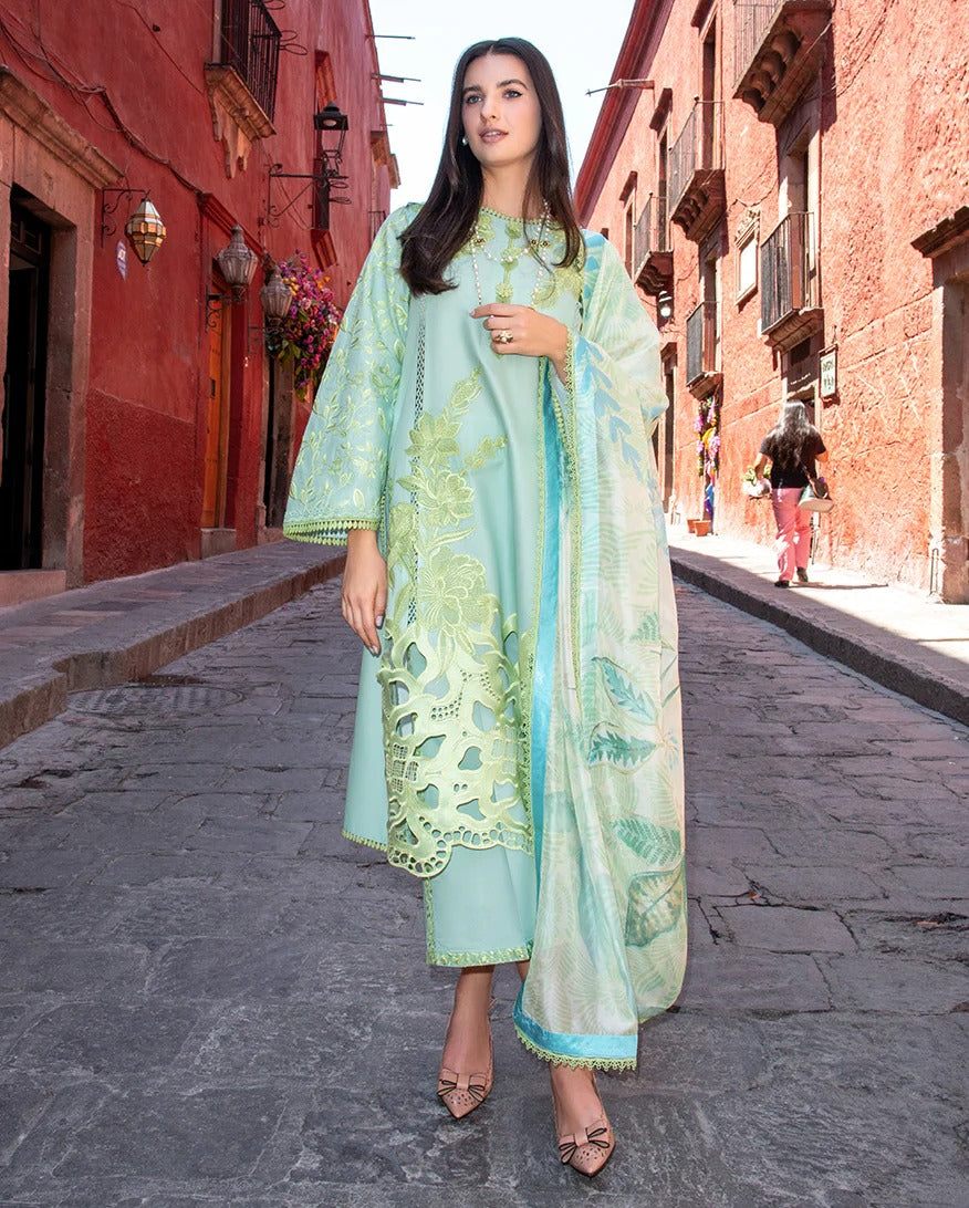 Woman in a light blue and green traditional outfit standing on a street with red buildings.