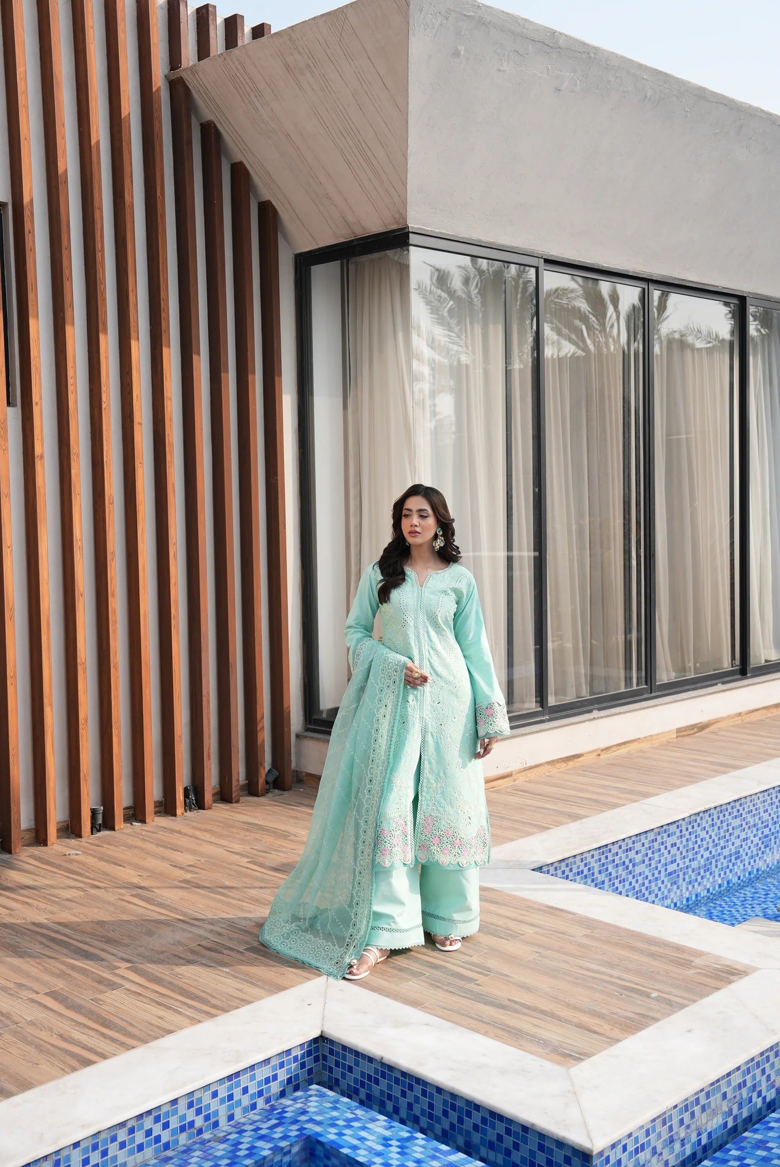 Woman in a light green traditional outfit standing by a modern building with a pool.