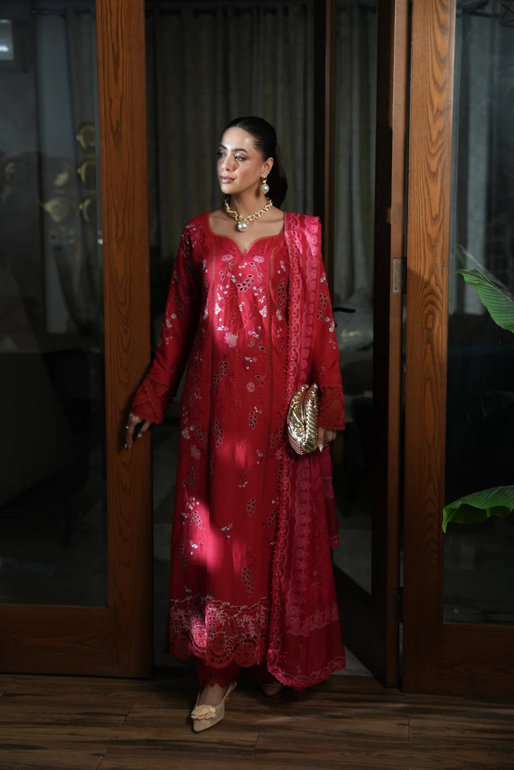 Woman in a red traditional outfit standing in front of a wooden door.