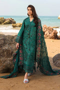 Woman in a teal embroidered outfit standing on a rocky beach with ocean in the background