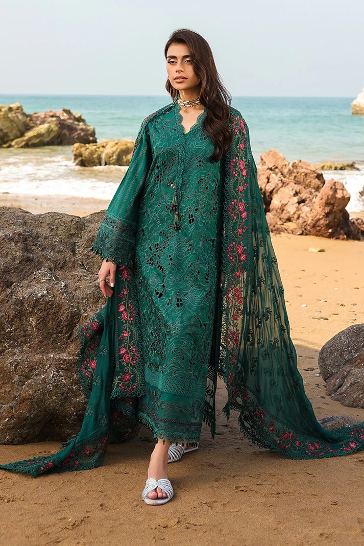 Woman in a teal embroidered outfit standing on a rocky beach with ocean in the background