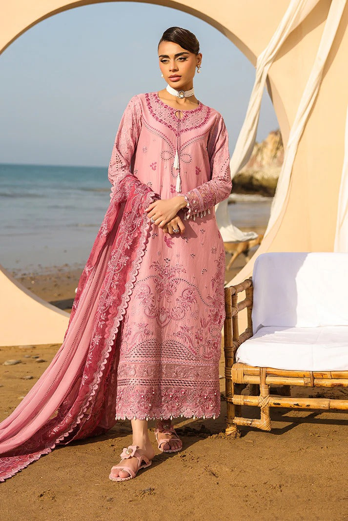 Woman in a pink embroidered outfit standing on a beach with ocean view.