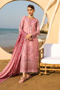 Woman in a pink embroidered outfit standing on a beach with ocean view.