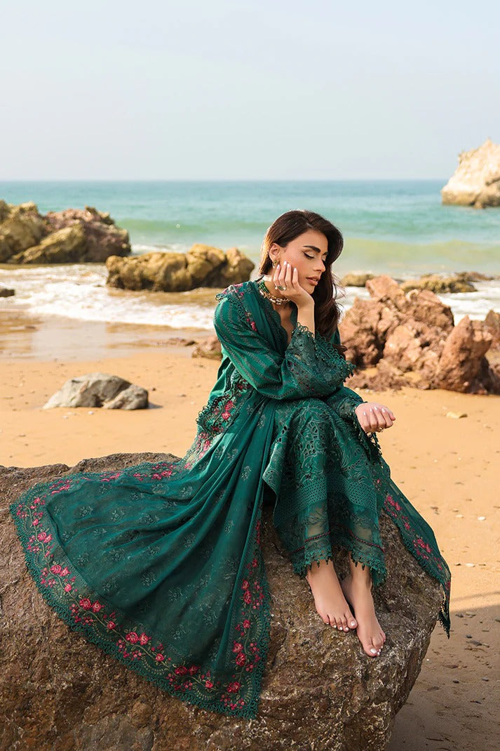 Woman in a green dress with floral embroidery sitting on a rock by the ocean.