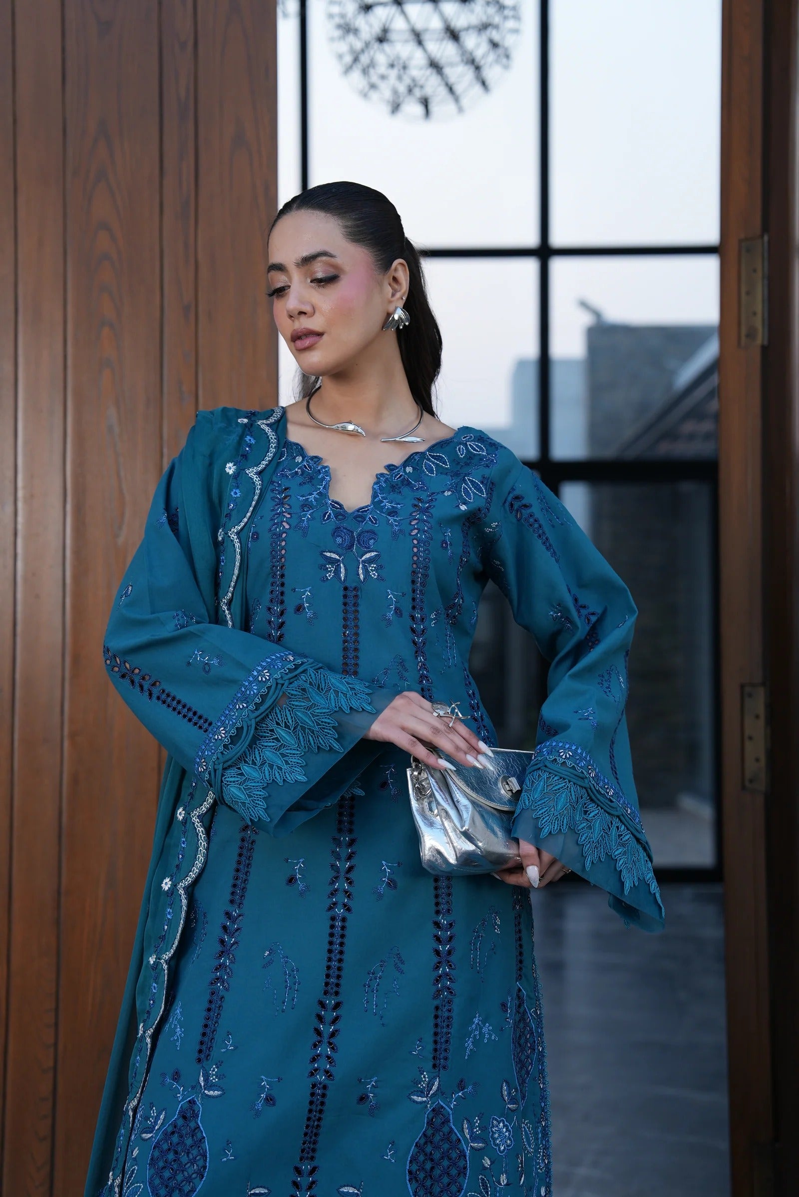 Woman in a blue embroidered dress standing indoors with a blurred background