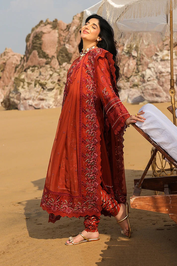 Woman in a red embroidered outfit standing in a desert with sand dunes and rocky formations in the background.