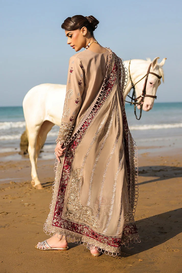 Woman in traditional outfit standing on a beach with a white horse in the background