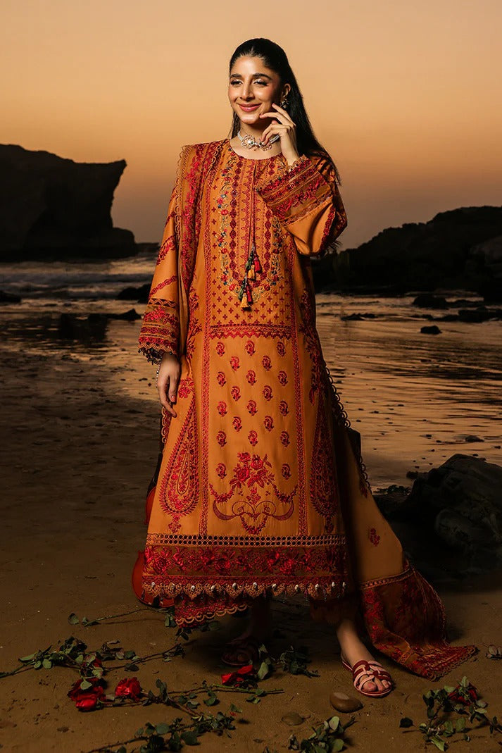 Woman in traditional orange and red embroidered outfit standing on a beach at sunset.