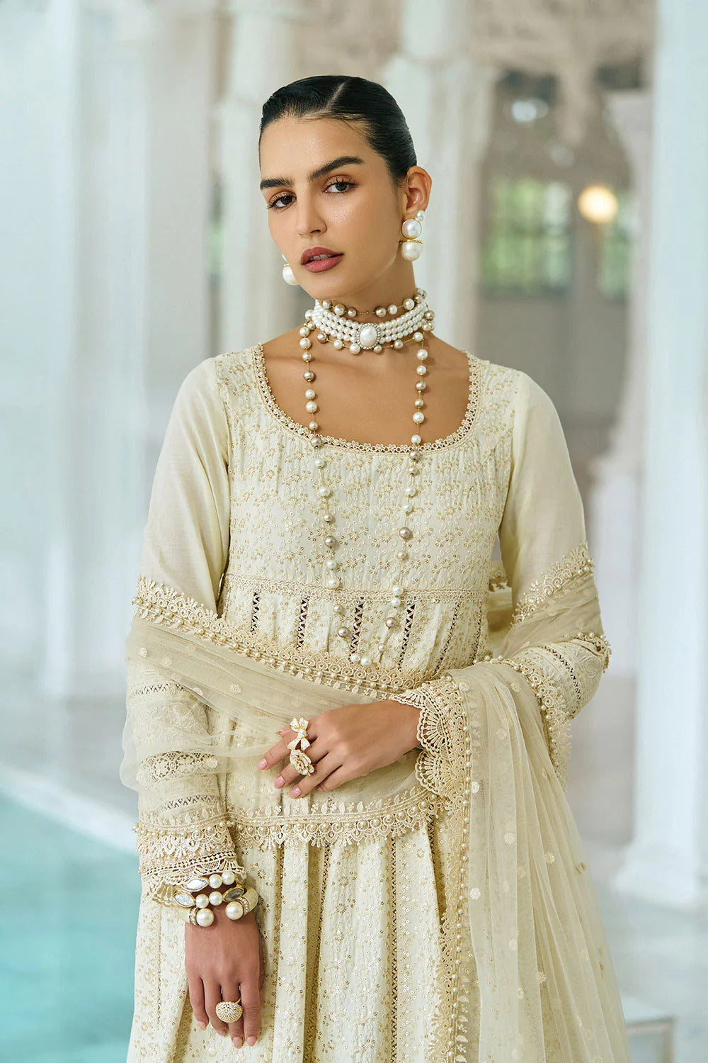 Woman wearing a cream traditional outfit with intricate detailing in an indoor setting.