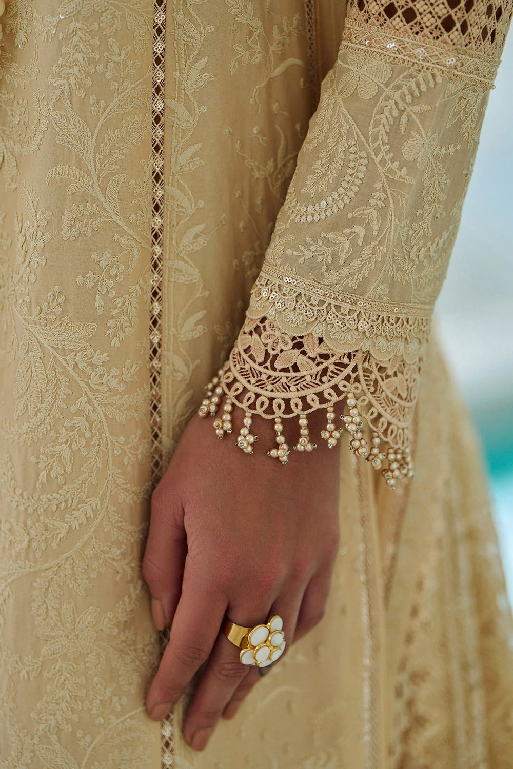 Close-up of a hand wearing a gold ring on beige embroidered fabric.