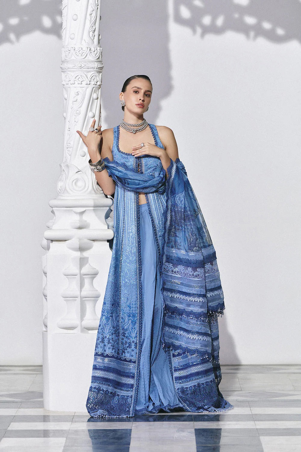 Woman in a blue saree standing against a white wall