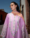 Woman wearing a purple embroidered outfit with a colorful scarf in an outdoor setting.