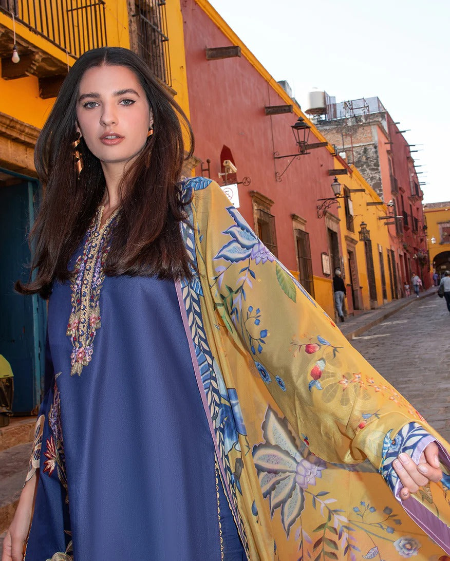 Woman wearing a blue dress with a yellow floral shawl in an urban setting