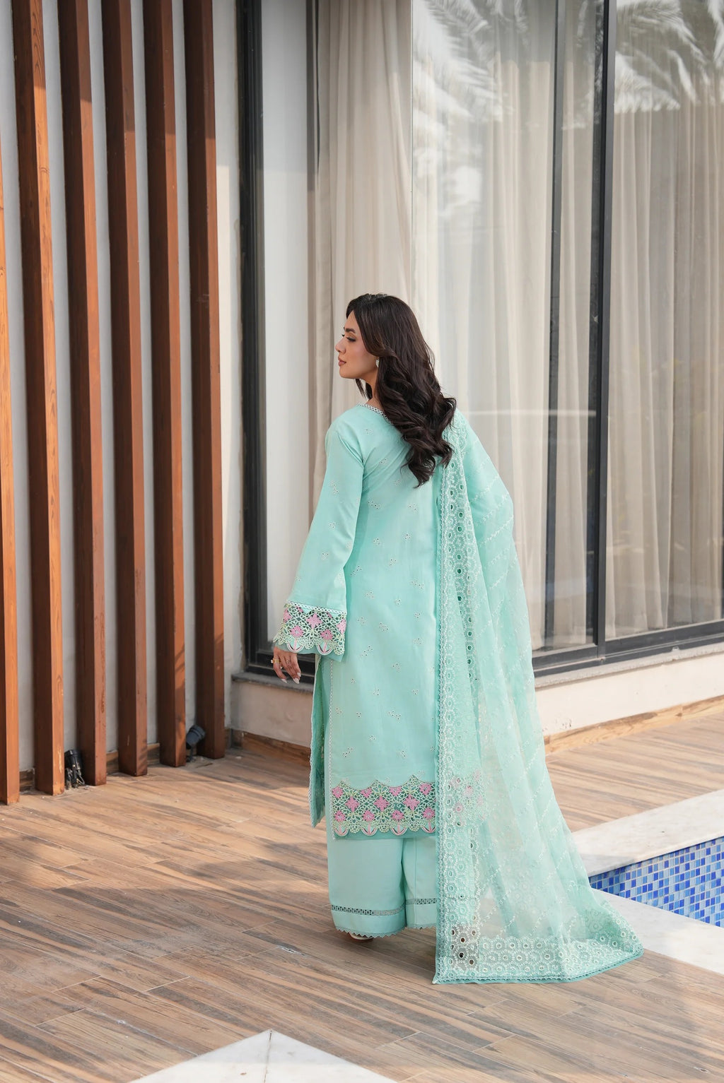 Woman in a light blue traditional outfit standing by a poolside.
