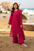 Woman in a pink traditional outfit standing on a beach with ocean waves in the background