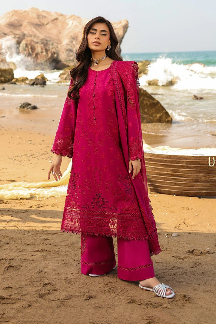 Woman in a pink traditional outfit standing on a beach with ocean waves in the background