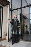 Woman in black traditional outfit with blue dupatta standing in a modern indoor setting.