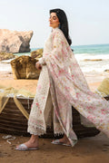 Woman in a floral dress standing on a beach with ocean and rocks in the background
