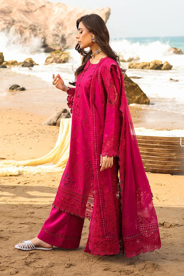 Woman in a pink traditional outfit standing on a beach with ocean waves in the background