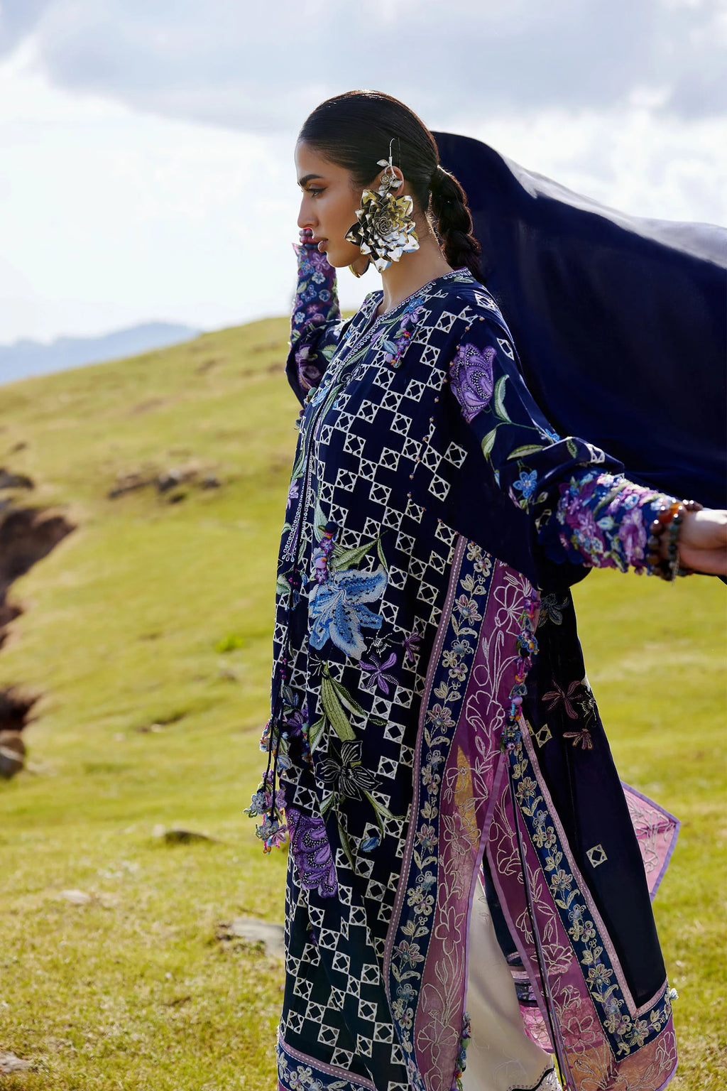 Woman in a patterned outfit standing in a grassy field with mountains in the background