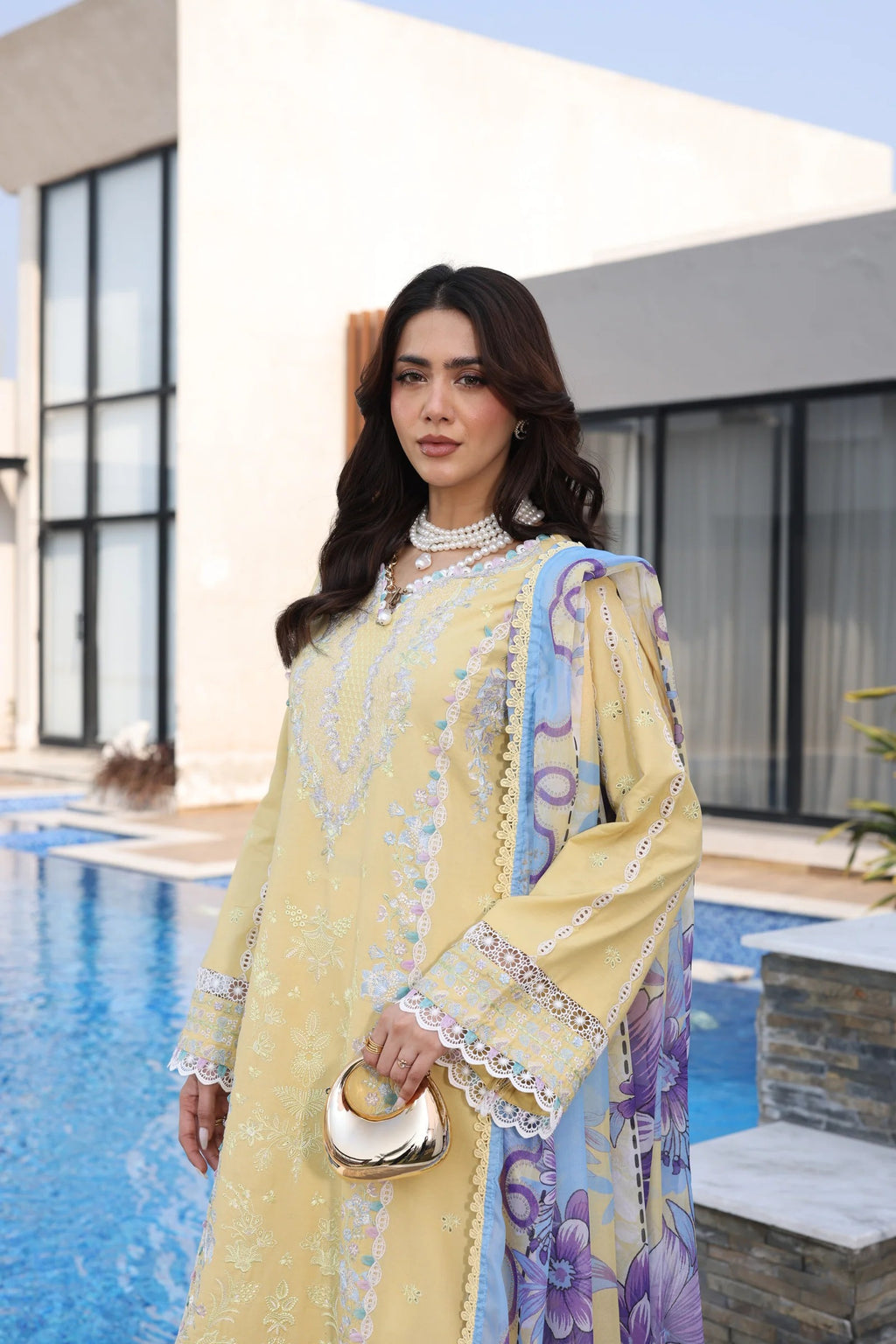 Woman in a yellow and blue traditional outfit standing by a pool.