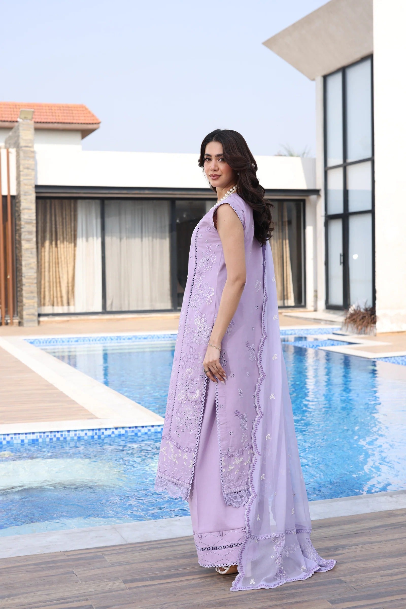 Woman in a lavender traditional outfit standing by a pool with a modern building in the background