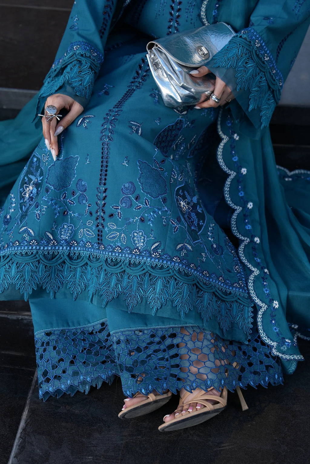 Person wearing a blue embroidered outfit holding a silver clutch.