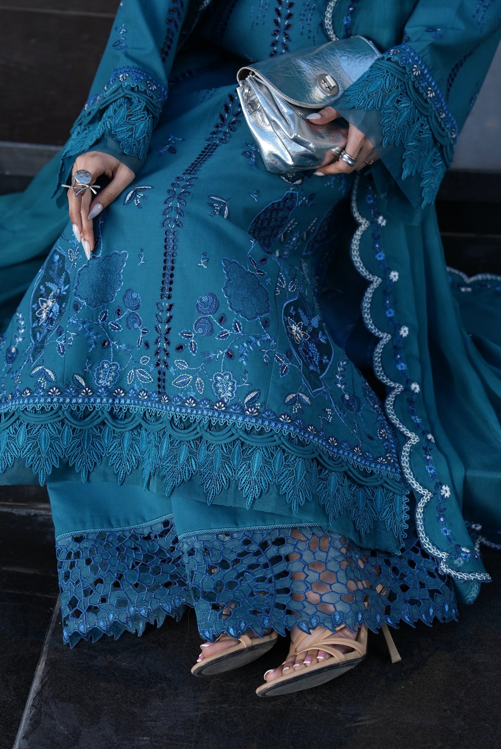 Person wearing a blue embroidered outfit holding a silver clutch.