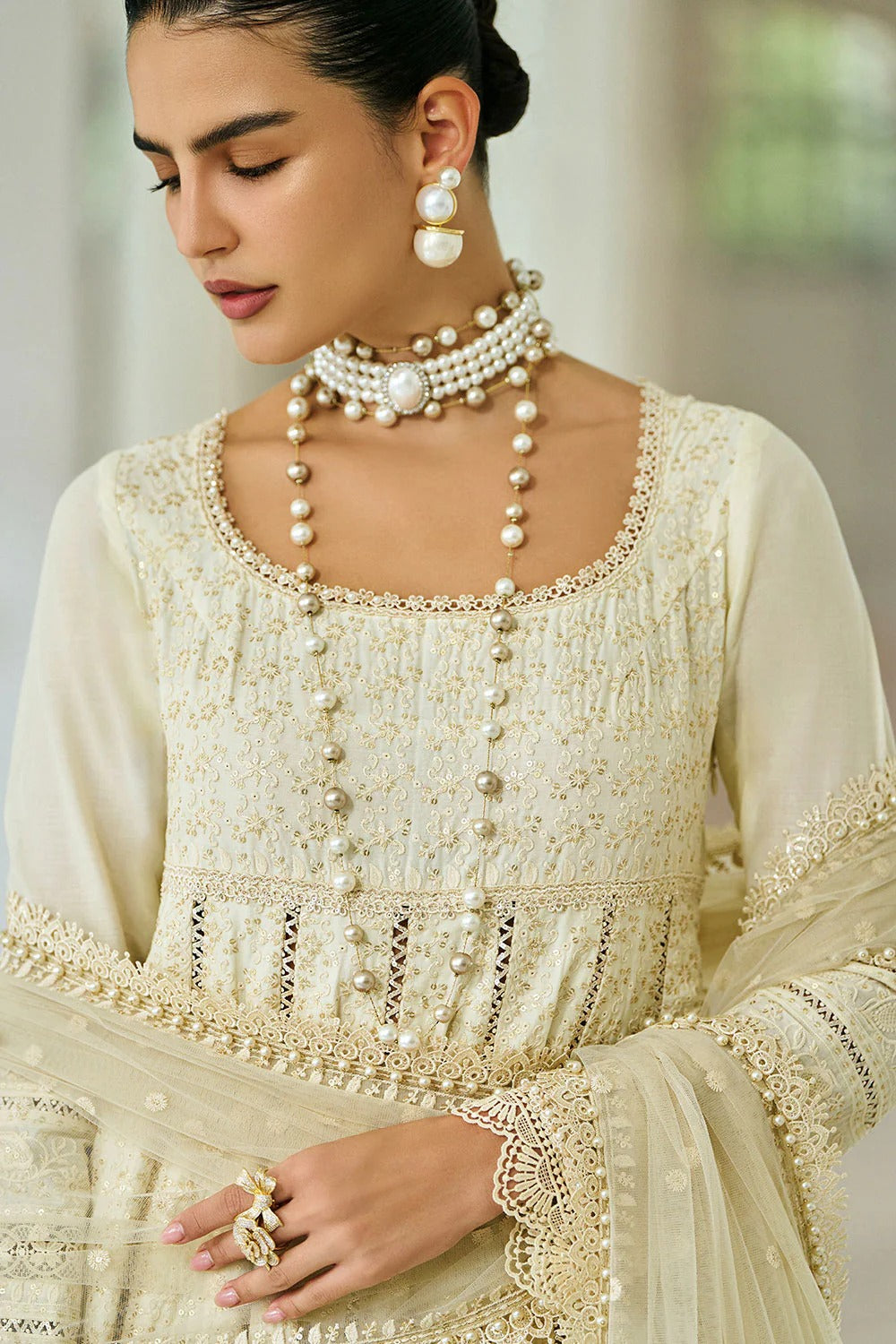 Woman wearing a cream-colored traditional outfit with intricate detailing and pearl jewelry.
