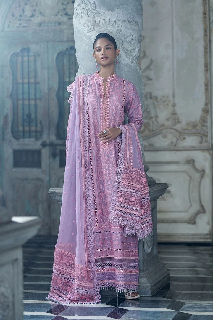Woman in a pink embroidered traditional outfit standing in an ornate interior setting.