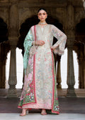 A woman models a traditional Indian salwar kameez suit with an embroidered light gray-green kurta, pink and green floral prints, and a mint green dupatta, set against a background of stone pillars.