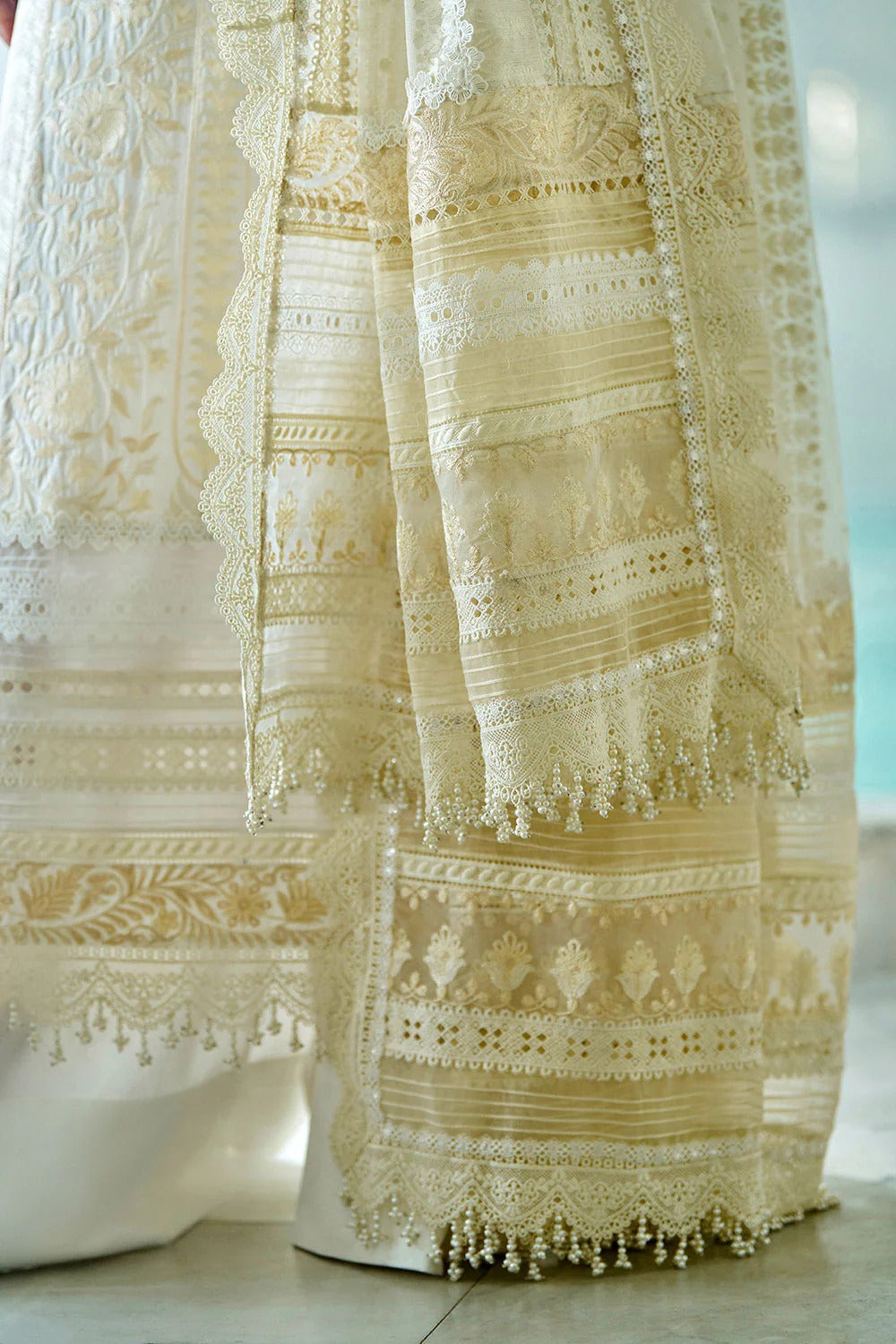 Close-up of a cream-colored lace curtain with intricate patterns and tassels.