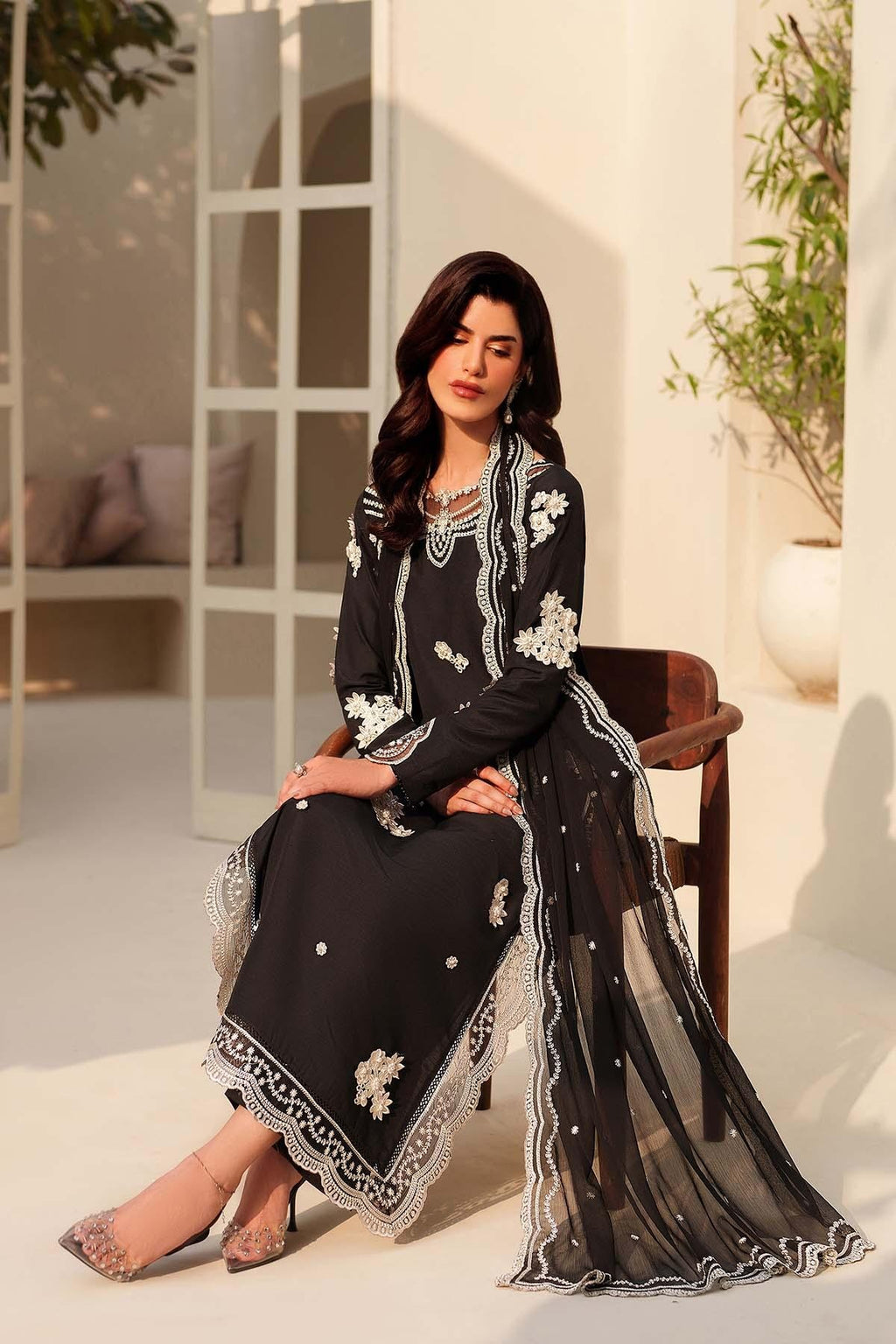 Woman in a black and white embroidered outfit sitting outdoors.