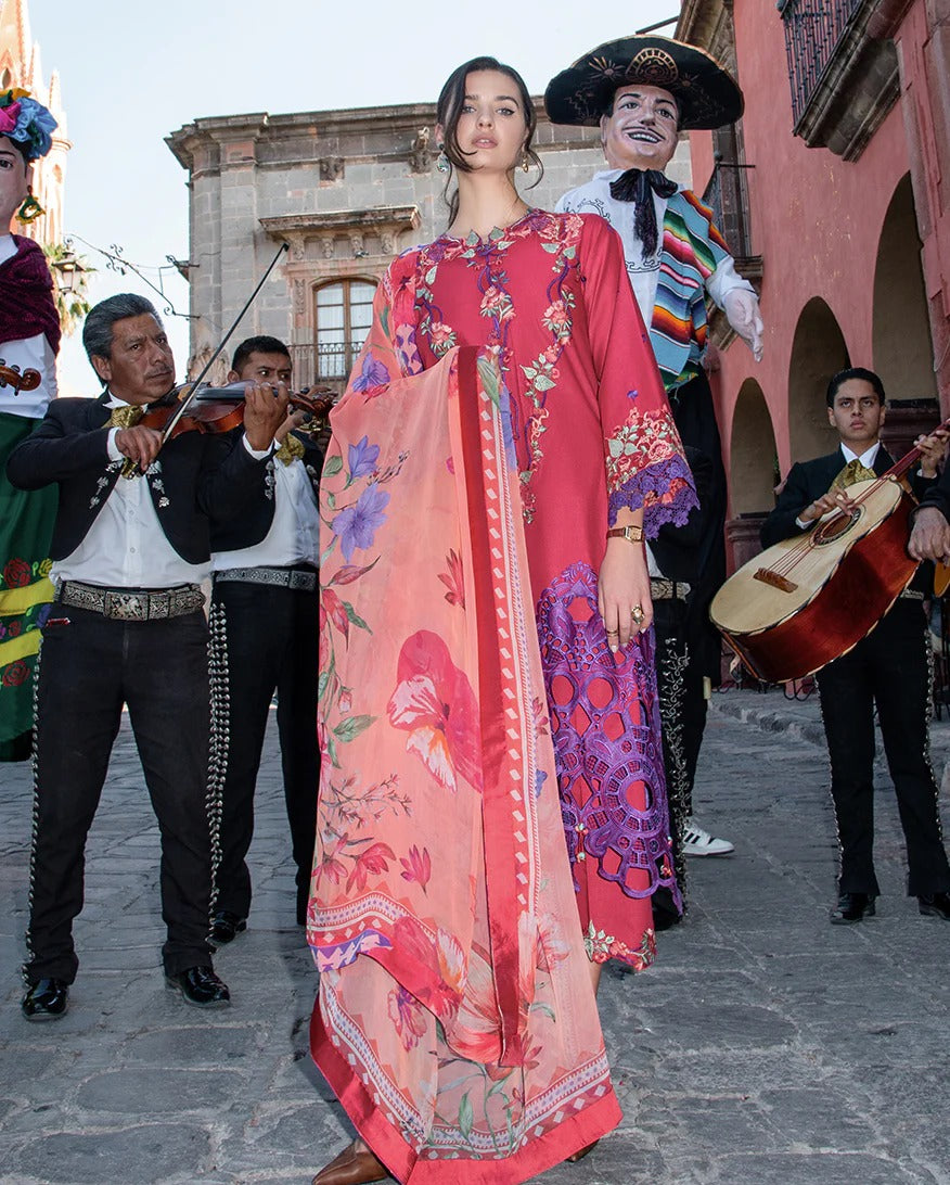 Woman in a colorful dress standing in front of a mariachi band with a pink building in the background.
