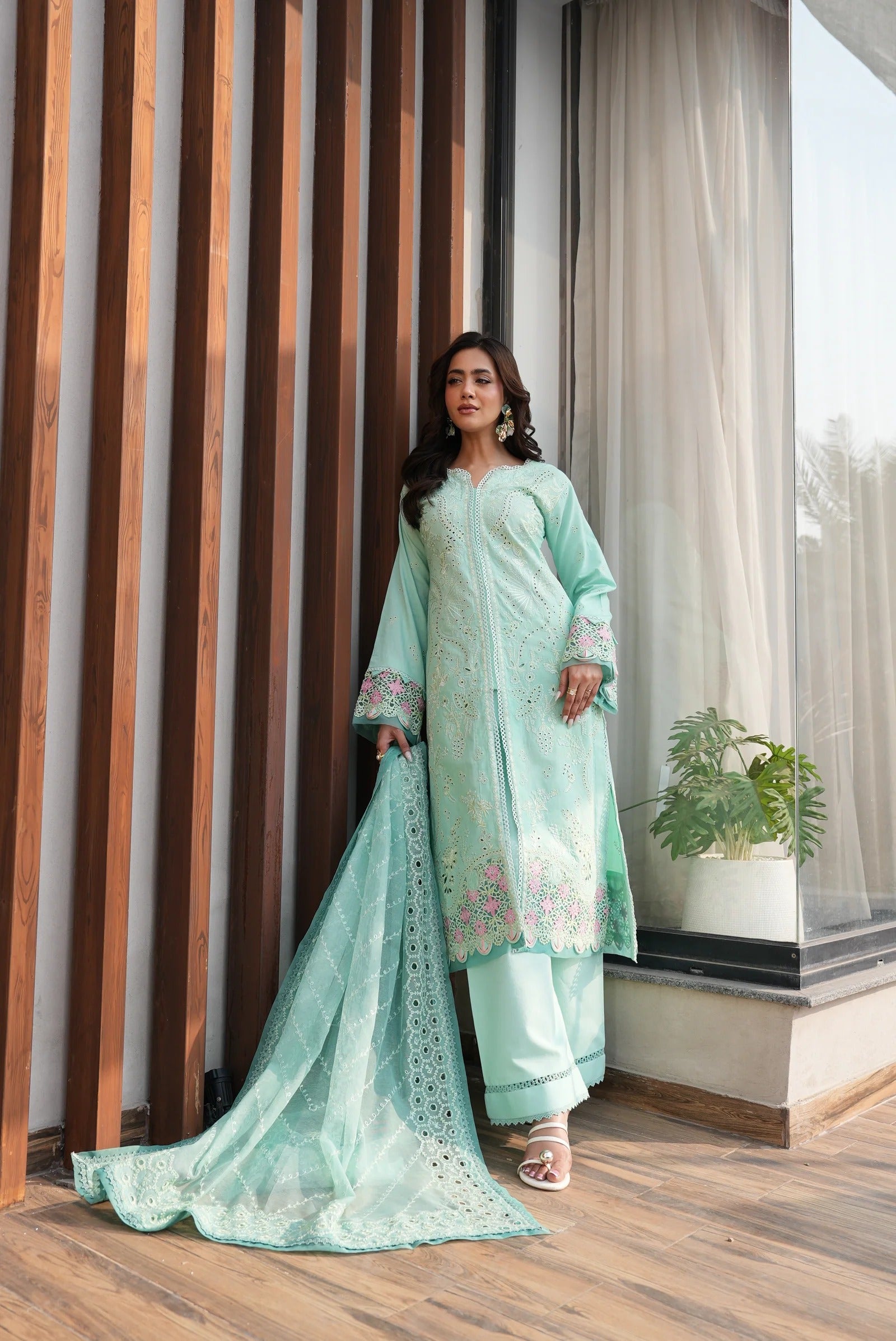 Woman in a light blue embroidered outfit standing indoors with wooden and glass walls.