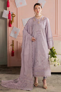 Woman in a lavender embroidered outfit standing in a room with pink walls and decorative elements.