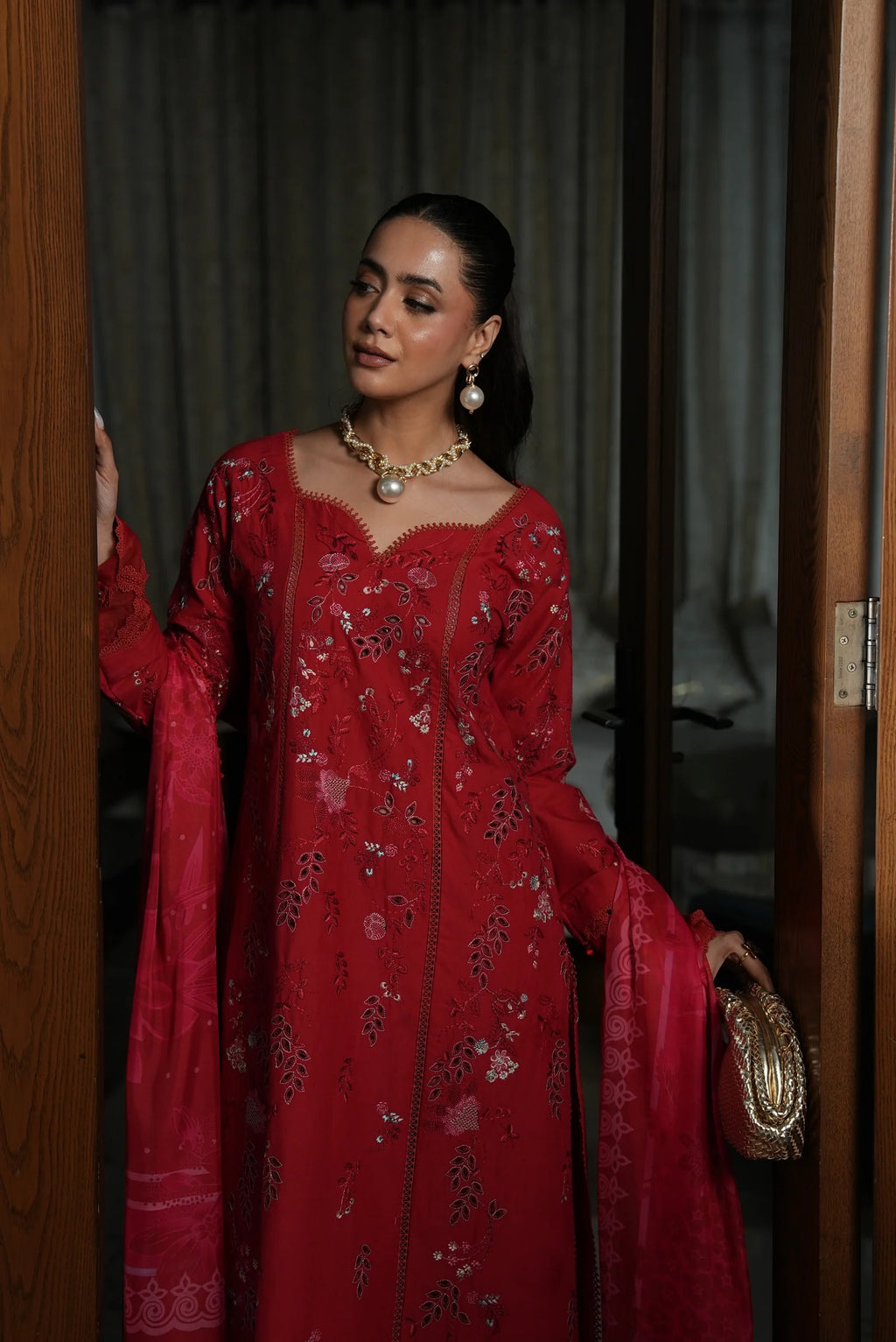 Woman in a red floral dress standing in a doorway.