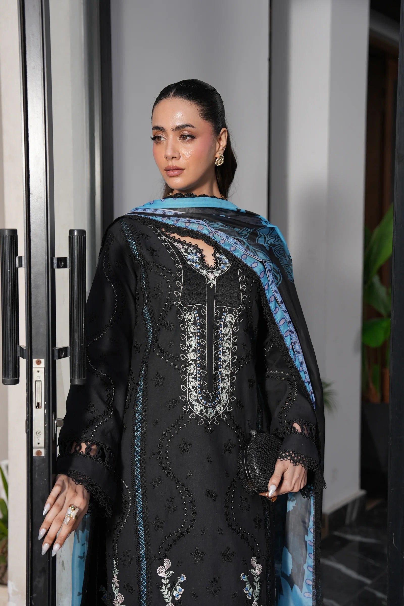 Woman wearing a black embroidered outfit with blue accents standing indoors.